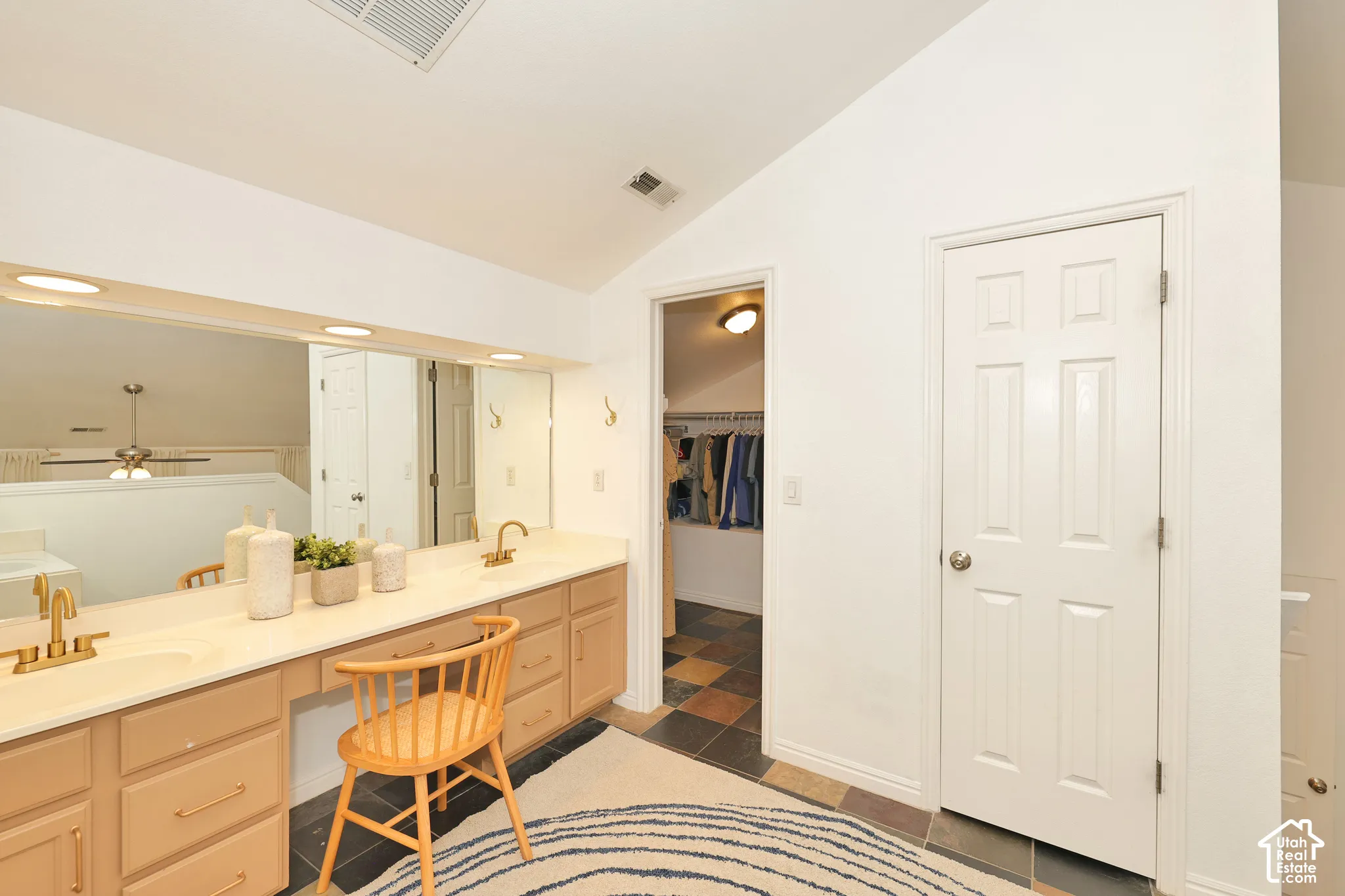 Vanity with dual integrated sinks, gold-tone faucets, wood-finish cabinetry, a large wall-mounted mirror, and multi-colored floor tiling