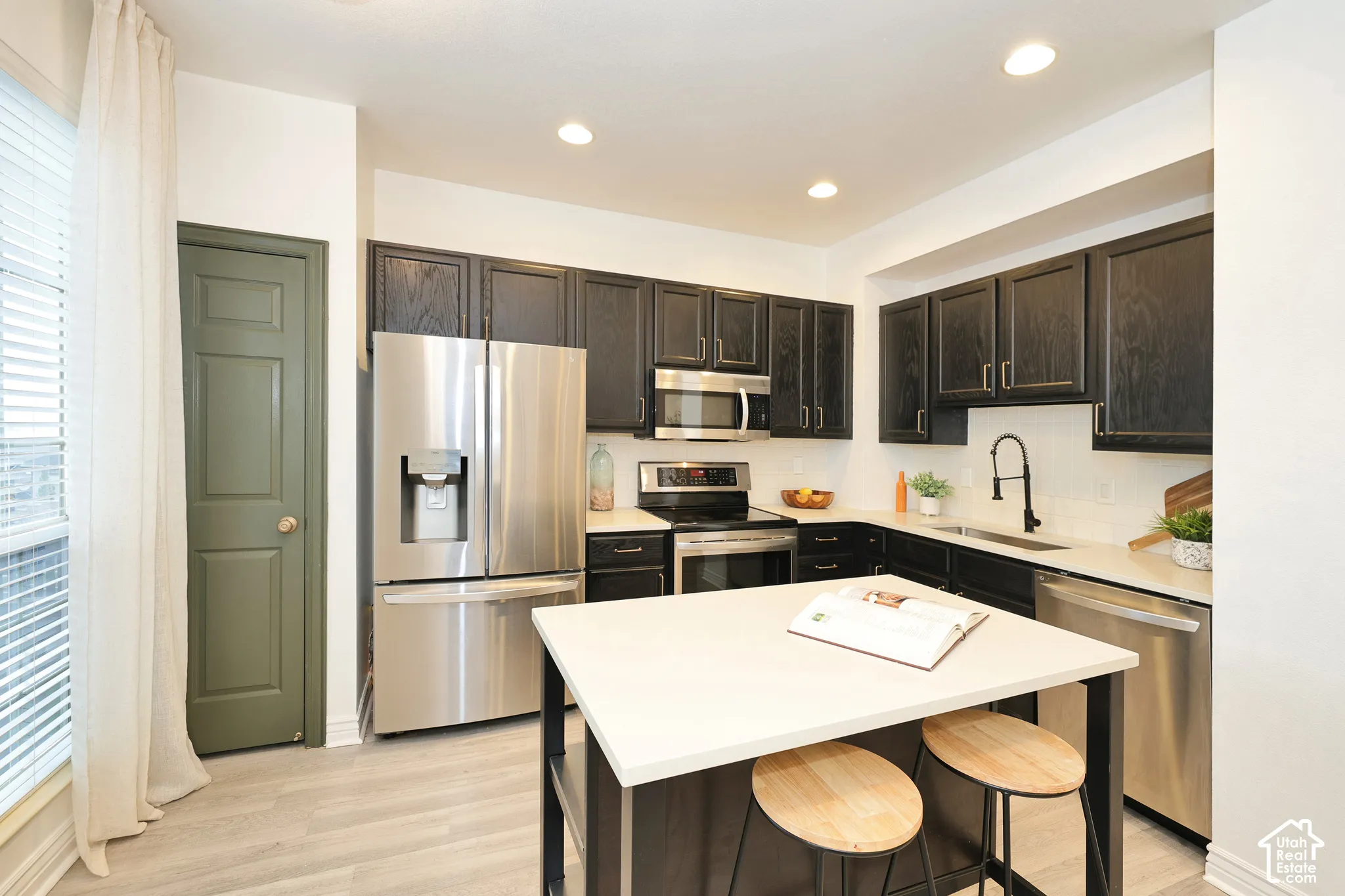 Kitchen featuring dark-finished cabinetry, stainless steel appliances, a central island with a light-toned countertop, and a matte black faucet