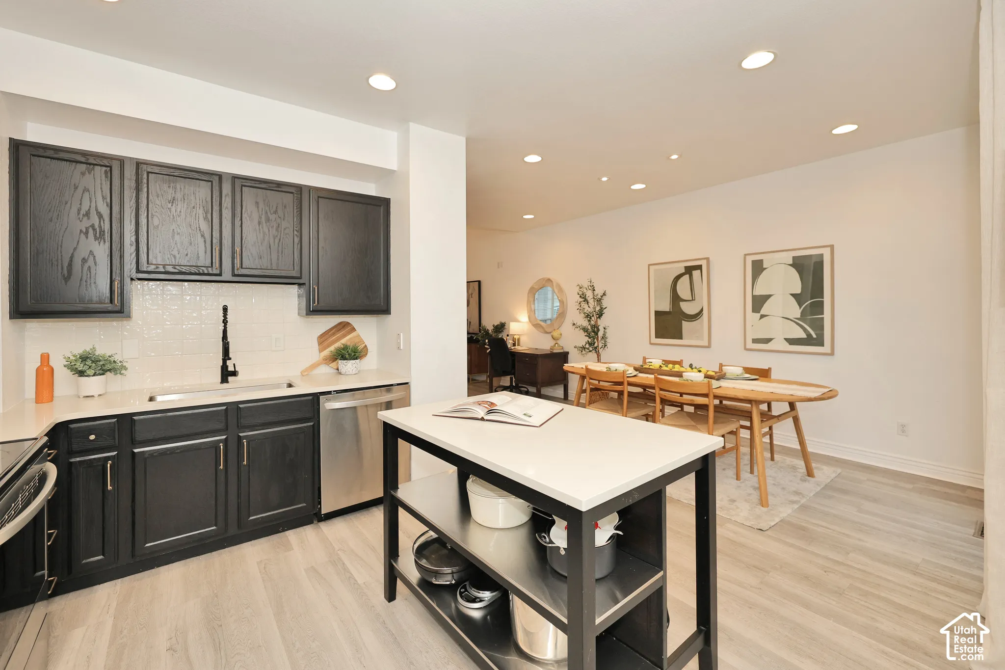 Kitchen featuring dark wood cabinetry, light-toned stone-finish countertops, tiled backsplash, stainless steel dishwasher, and a central island with integrated open shelving
