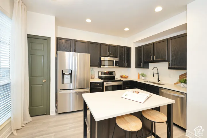 Kitchen featuring dark-finished cabinetry, stainless steel appliances, a central island with a light-toned countertop, and a matte black faucet