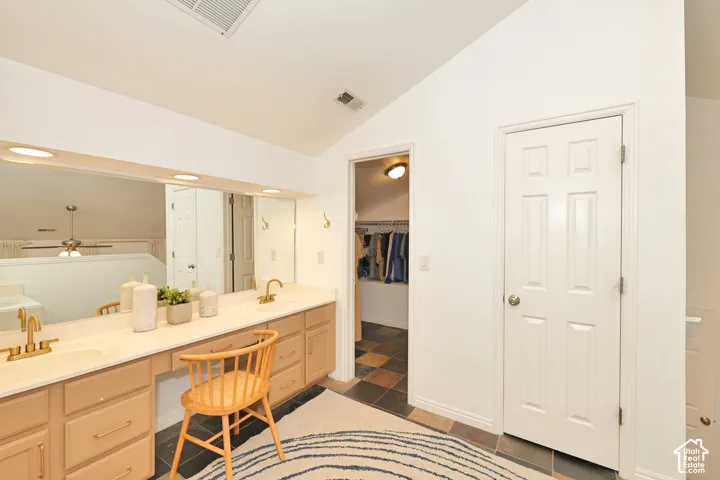 Vanity with dual integrated sinks, gold-tone faucets, wood-finish cabinetry, a large wall-mounted mirror, and multi-colored floor tiling