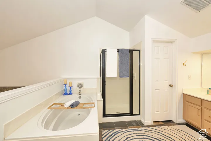 Bathroom featuring a vaulted ceiling, a built-in soaking tub, and a glass-enclosed shower with a black frame