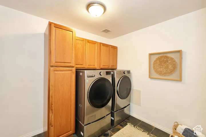 Utility room featuring natural wood-finish cabinetry, floor-to-ceiling storage, and dark stone-tile flooring