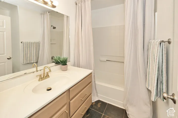 Bathroom featuring a wood-finish vanity with an integrated basin, brushed metal faucet, full-width vanity mirror, and stone-finish floor tiling