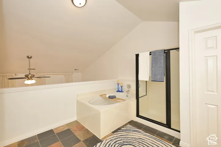 Soaking tub with a solid surface surround, glass-enclosed shower with black metal framing, vaulted ceiling, and multi-tonal tile flooring