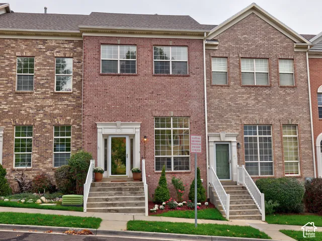 Multi-story brick exterior featuring gable roof lines, white architectural door trim, multi-pane windows, and concrete front entry staircases with white railings