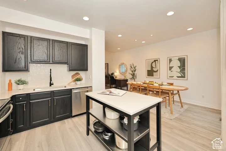 Kitchen featuring dark wood cabinetry, light-toned stone-finish countertops, tiled backsplash, stainless steel dishwasher, and a central island with integrated open shelving