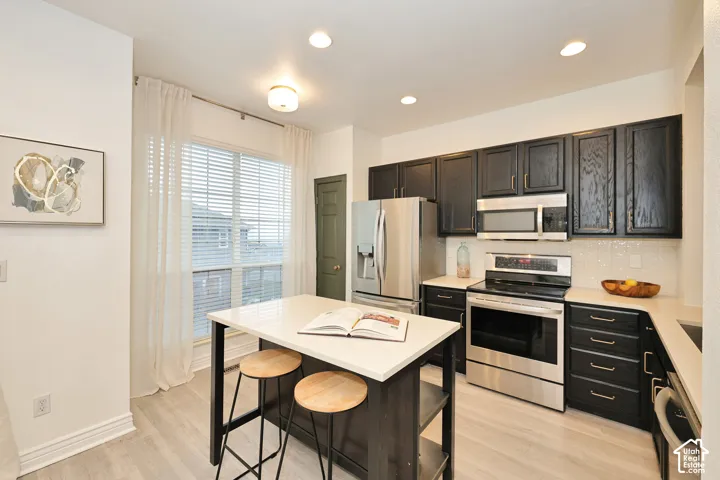 Kitchen featuring dark cabinetry, quartz countertops, a central island, stainless steel appliances, and wood-finish flooring