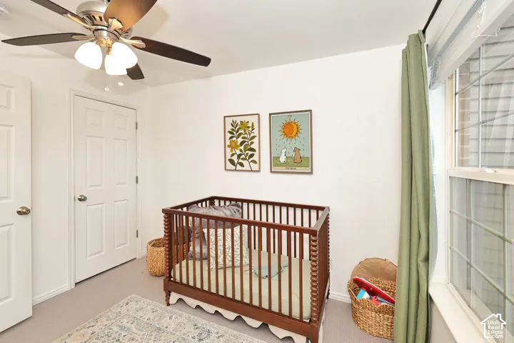 Bedroom featuring neutral wall-to-wall carpeting, a ceiling fan with integrated lighting, and a multi-pane window