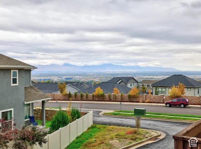 Exterior perspective featuring mountain and valley scenery, concrete-paneled siding, a stone masonry retaining wall, and vinyl perimeter fencing