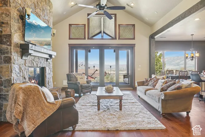 Stone-clad fireplace with mantel, vaulted ceiling with exposed beam, wood-finish flooring, and glass doors to an exterior space