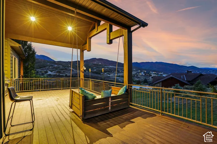 Expansive wood-finish deck with a built-in swing, illuminated by attached overhead lighting, and featuring metal railings