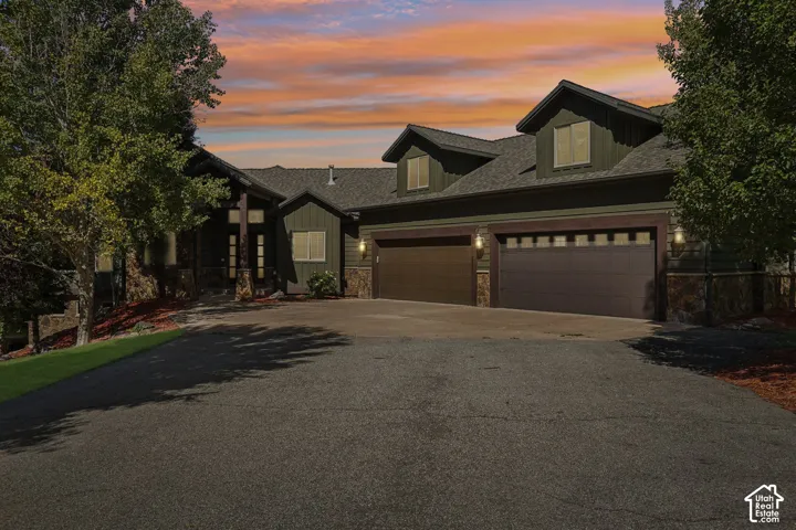 Multi-level exterior featuring dormer windows, a two-car garage with transom windows, stone veneer accents, and a paved driveway