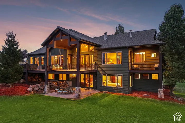 Multi-level exterior with a large second-story deck, ground-level patio, expansive lawn, and architectural wood beam accents