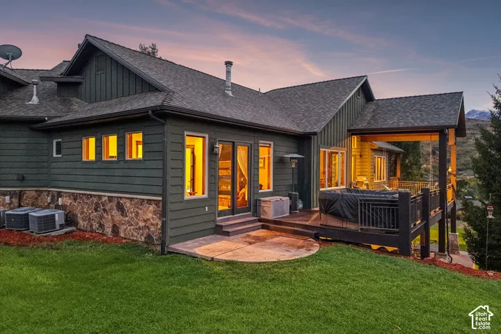 Multi-level exterior with dark green horizontal siding and a stone-clad foundation