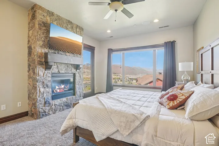 Stone-clad fireplace with mantel, recessed lighting, ceiling fan, and large windows