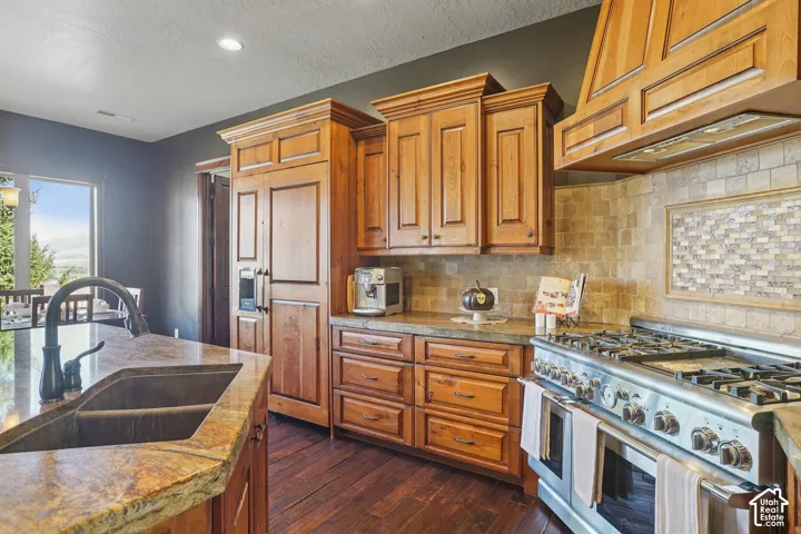Wood-finish flooring, full-height wood cabinetry, stainless steel range, built-in refrigerator, and stone countertops