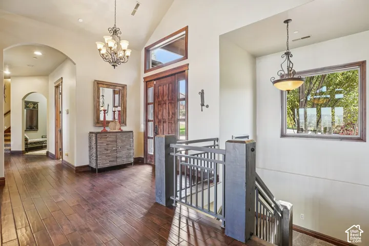 Wood-finish flooring throughout, vaulted ceiling, arched doorway, and a prominent staircase with metal railings
