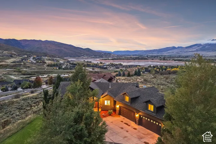 Expansive mountain and water scenery, multi-car garage, dormer windows, natural wood siding, and established landscaping