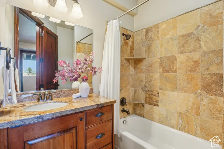 Vanity with a polished stone countertop, undermount sink, and wood-finish cabinetry with dark hardware