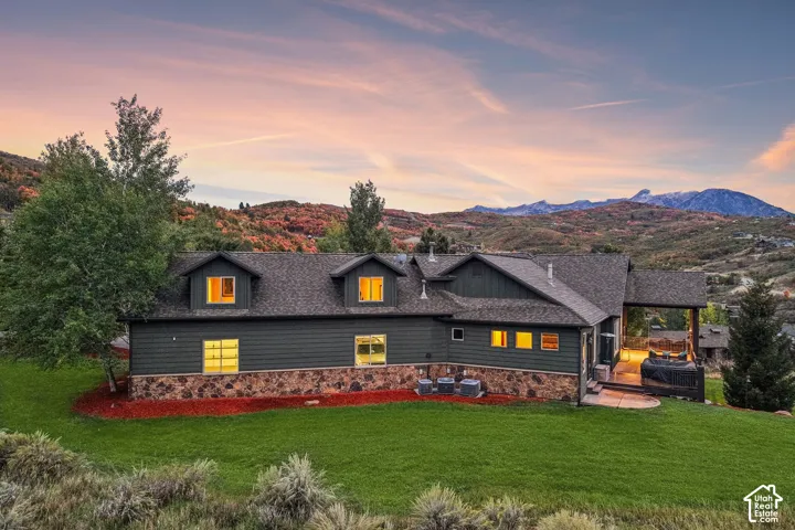 Stone and siding exterior with dormer windows, covered patio, and manicured lawn