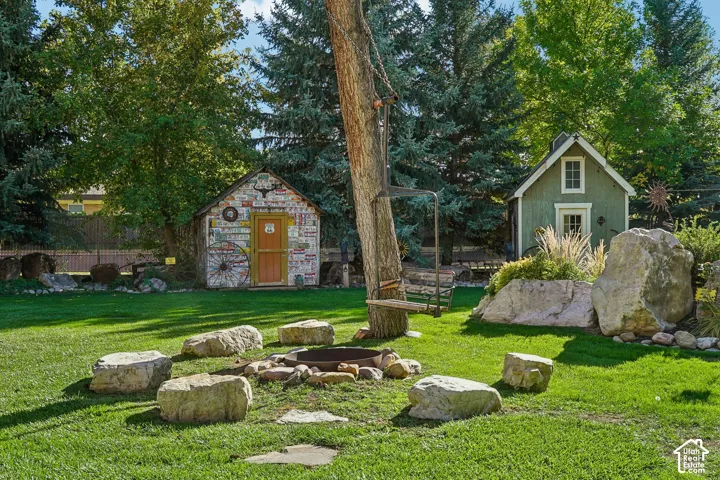 Expansive backyard featuring a lush lawn, built-in fire pit with stone seating, and two distinct accessory structures