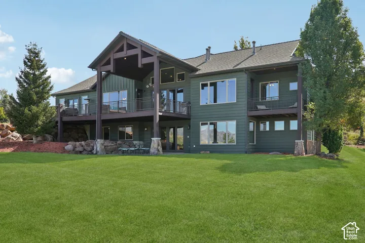 Expansive green lawn with a multi-story exterior, multiple balconies, and a stone-accented patio