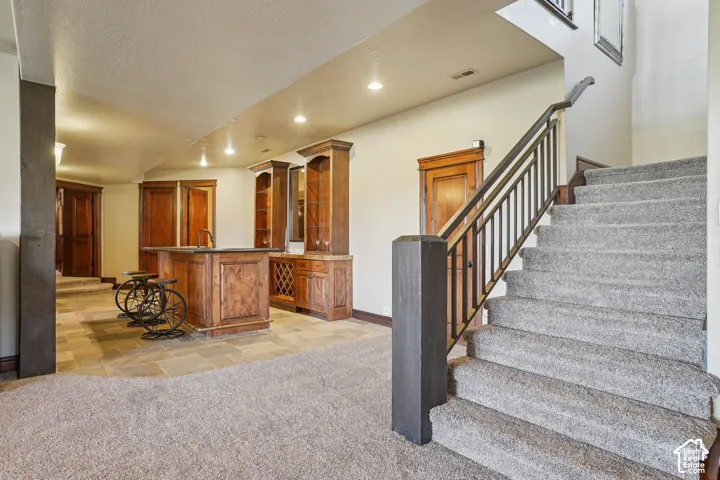 Lower level featuring a built-in wet bar with wood cabinetry, stone countertop, and integrated sink