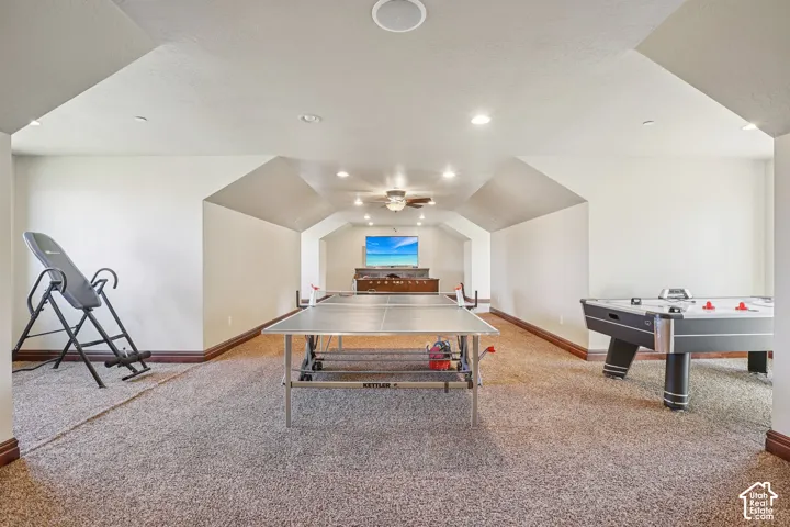 Expansive carpeted room with recessed lighting and a ceiling fan, featuring sloped ceiling elements