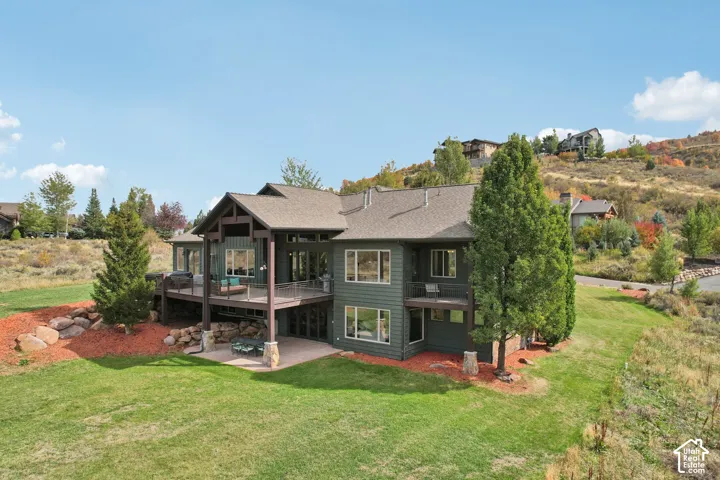 Multi-level residence featuring a covered deck, stone accents, expansive windows, and a lower-level patio