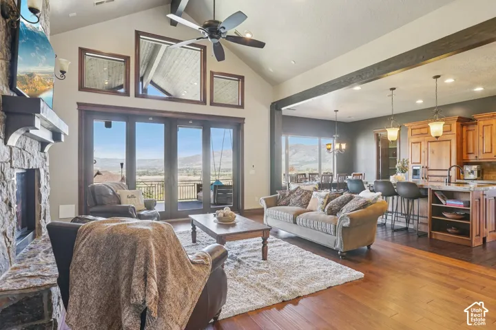 Vaulted ceilings with exposed beams, stone fireplace, wood-finish flooring, and a kitchen island with pendant lighting