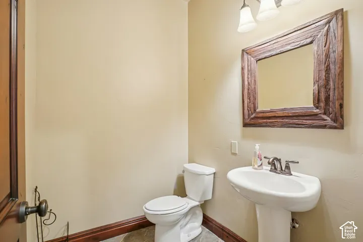 Pedestal sink, wall-mounted mirror with a rustic frame, three-light vanity fixture, and a toilet