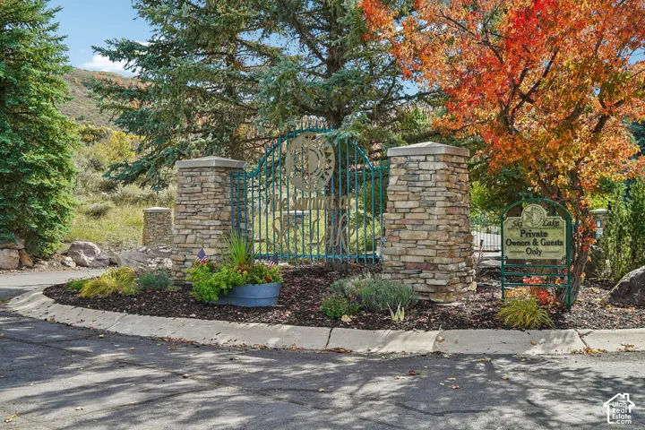 Stone-clad entry pillars, decorative metal gate, and mature trees with autumn foliage