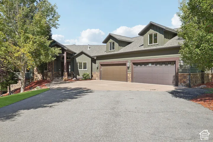 Paved driveway leading to a residence featuring a stone and siding exterior, a front entry with columns, and a two-car garage with dormer windows above