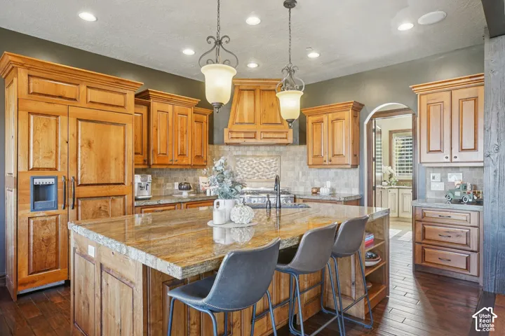 Kitchen featuring wood cabinetry, a large center island with stone countertop, wood-finish flooring, a tile backsplash, and recessed lighting