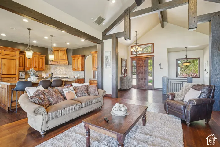 Vaulted ceilings with exposed beams, hardwood flooring, kitchen with light wood cabinetry, stone countertops, and a decorative tile backsplash
