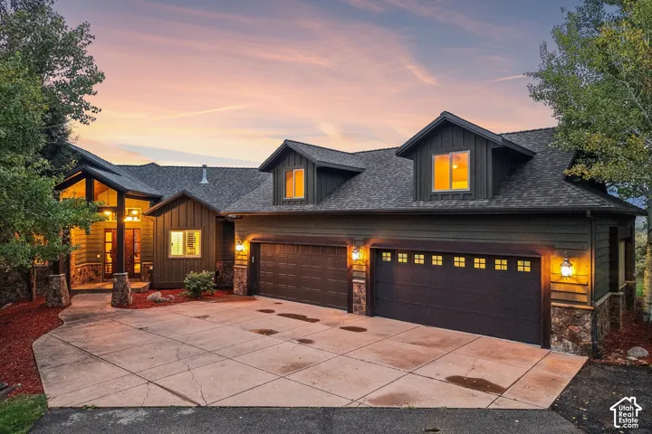 Multi-car driveway with integrated garage, dormer windows, natural wood siding, and stone accents
