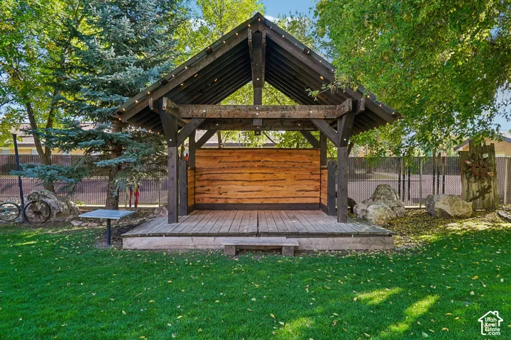 Expansive outdoor gazebo with a wood deck and a natural wood accent wall, surrounded by mature trees and a manicured lawn