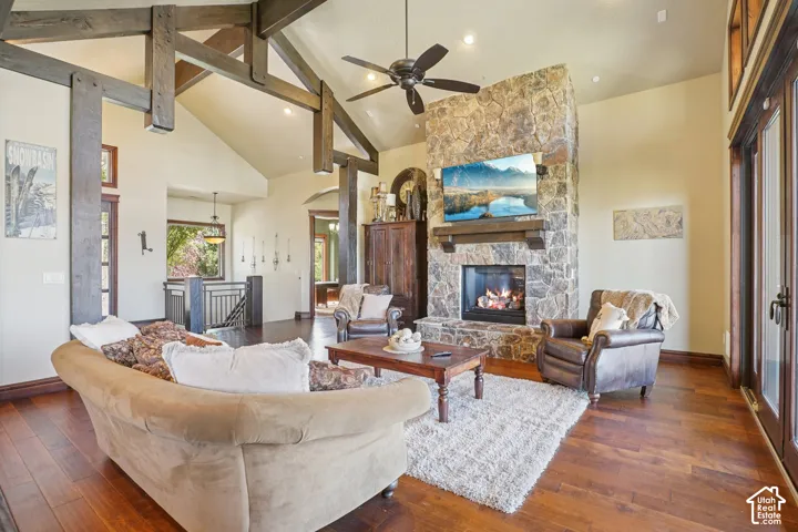 Vaulted ceilings with exposed wood beams, a stone fireplace with a wood mantel, rich wood-finish flooring, and double French doors