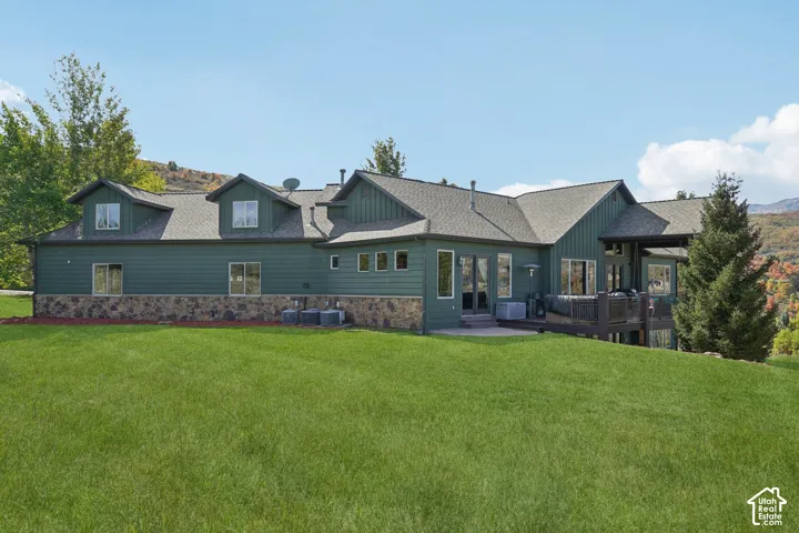 Expansive grass lawn with a multi-level exterior featuring a stone foundation and wood siding