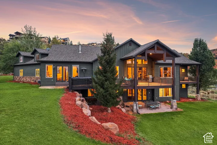 Expansive multi-level deck, lower patio area, stone accent siding, large windows, and a surrounding green lawn
