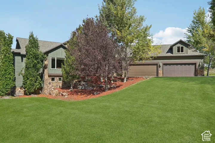 Stone and siding exterior with a multi-car garage, dormer window, and mature landscaping
