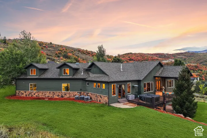 Expansive green lawn, dark green siding, stone accent base, multi-level exterior deck, and dormer windows