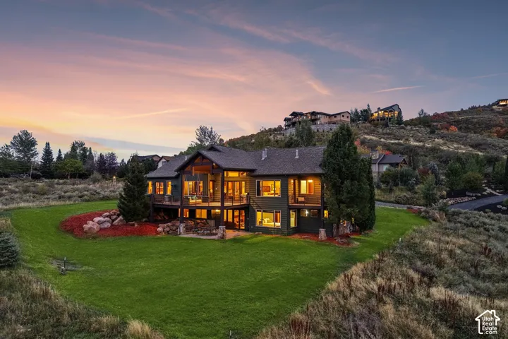 Multi-level residence featuring a large deck, lower patio, pitched roof, and expansive lawn
