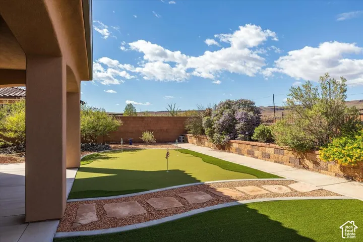 Covered patio featuring a backyard putting green, artificial turf, stone paver pathway, and stacked stone retaining wall