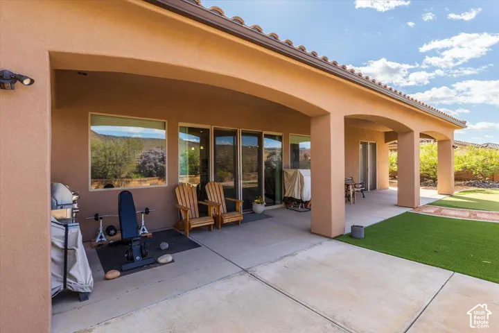 Covered concrete patio with arched structural columns, stucco exterior finish, clay tile roofline, and low-maintenance synthetic turf yard