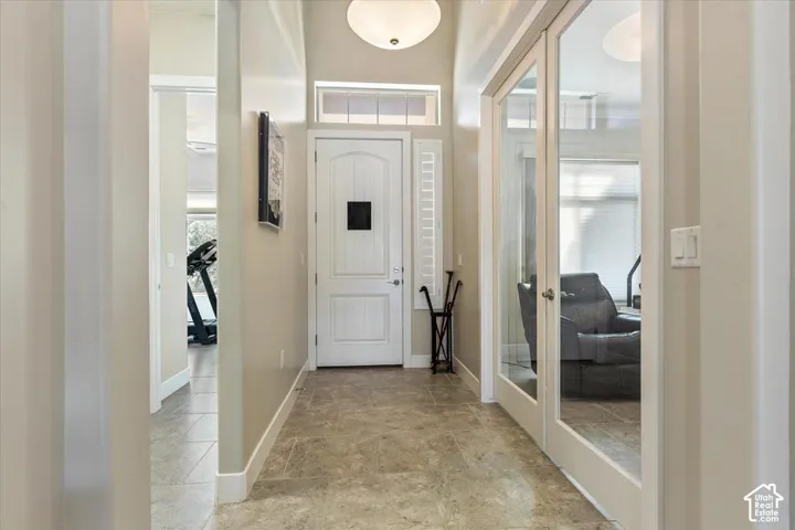 Entryway featuring high ceilings, neutral stone-finish tile flooring, a solid core door with a transom window, and dual glass-panel French doors