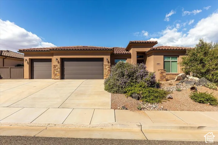 Stucco exterior featuring stacked stone accents, a multi-car garage, and a tile roof, complemented by xeriscaped front landscaping