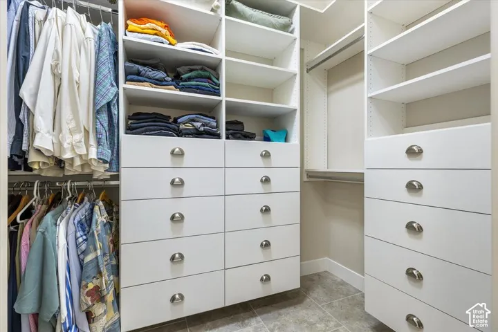 Walk-in closet featuring white built-in cabinetry, multiple adjustable shelving units, integrated chest of drawers with brushed metal pulls, and tile flooring