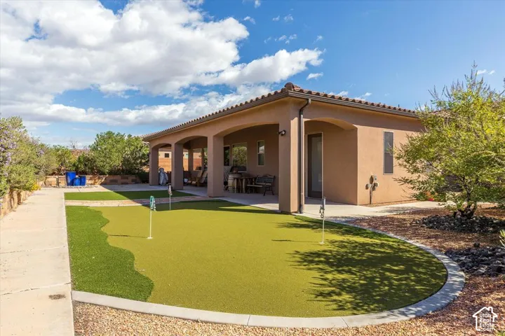 Stucco exterior featuring a covered patio, artificial turf putting green, concrete walkways, and desert landscaping